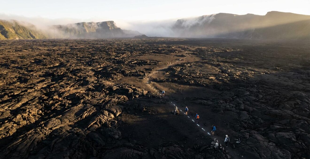 Vue panoramique de l'Enclos Fouqué avec des randonneurs sur les sentiers balisés traversant les champs de lave noire