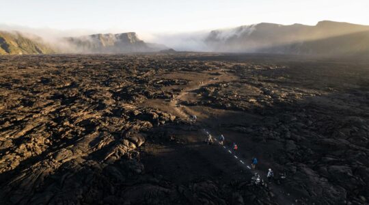 Vue panoramique de l'Enclos Fouqué avec des randonneurs sur les sentiers balisés traversant les champs de lave noire